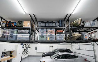 Overhead garage storage racks mounted to the ceiling, holding labelled bins and seasonal gear above the parked cars.