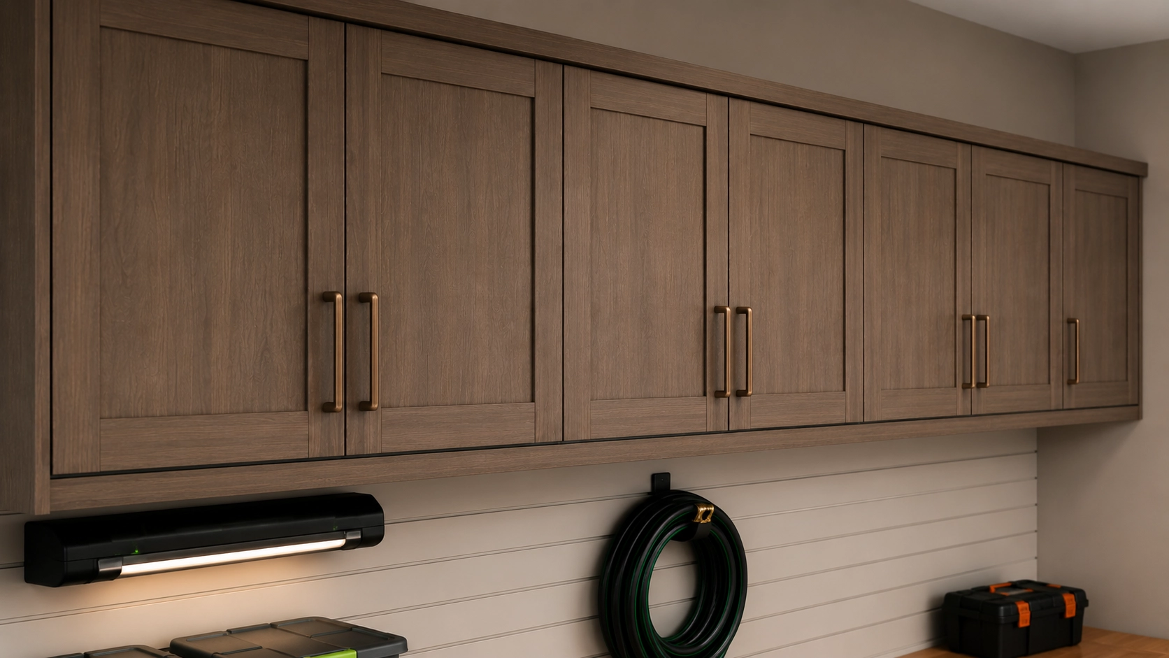 Wall-mounted garage cabinets in a grey-brown woodgrain finish above a white slatwall with hanging storage.