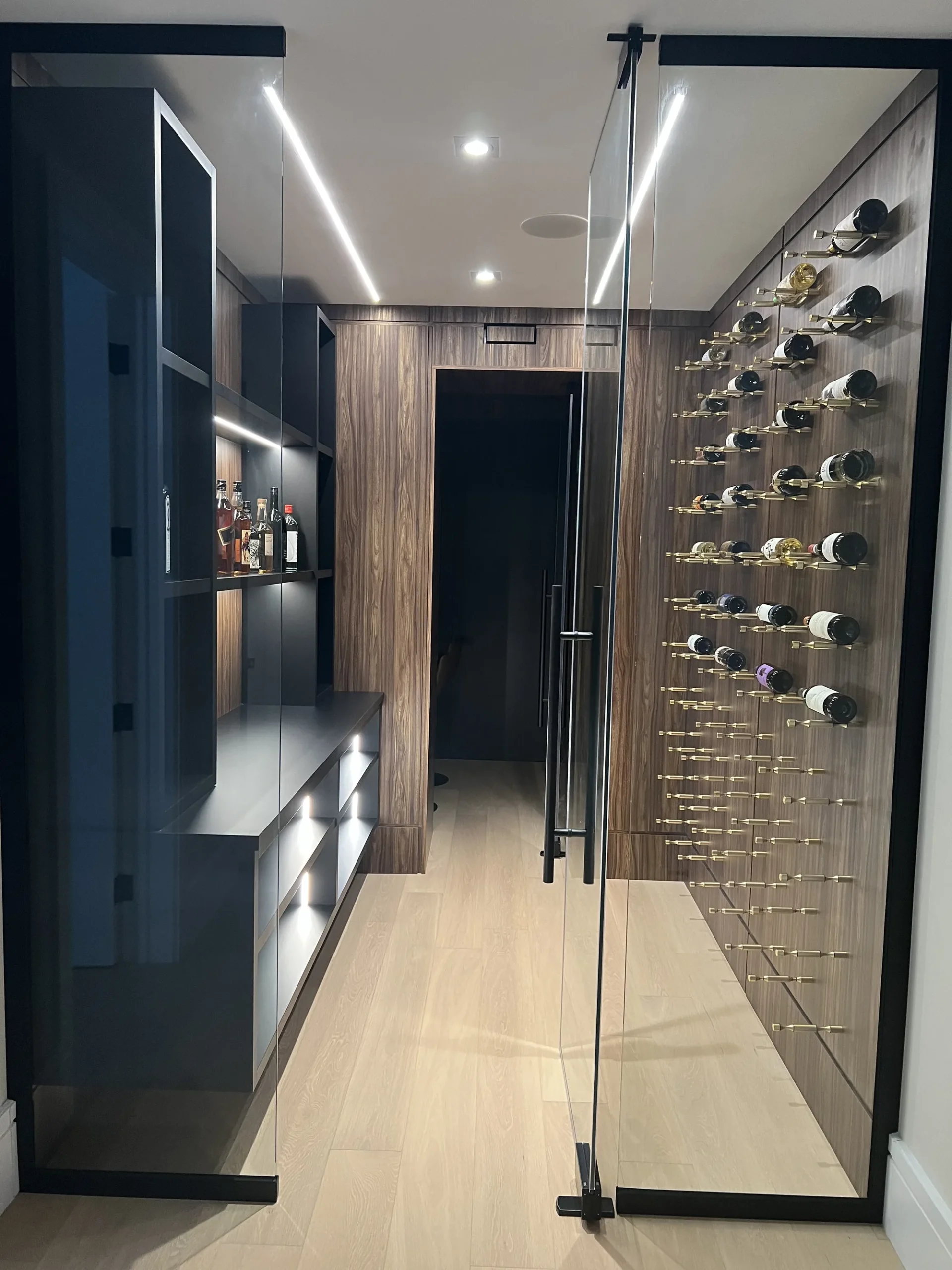 Canadian-Made Custom Cabinetry & Built-In Furniture 1 Canadian-made cabinetry in an Ontario home: a glass-enclosed wine room with walnut wall panels, brass peg racking and an integrated bar shelf.