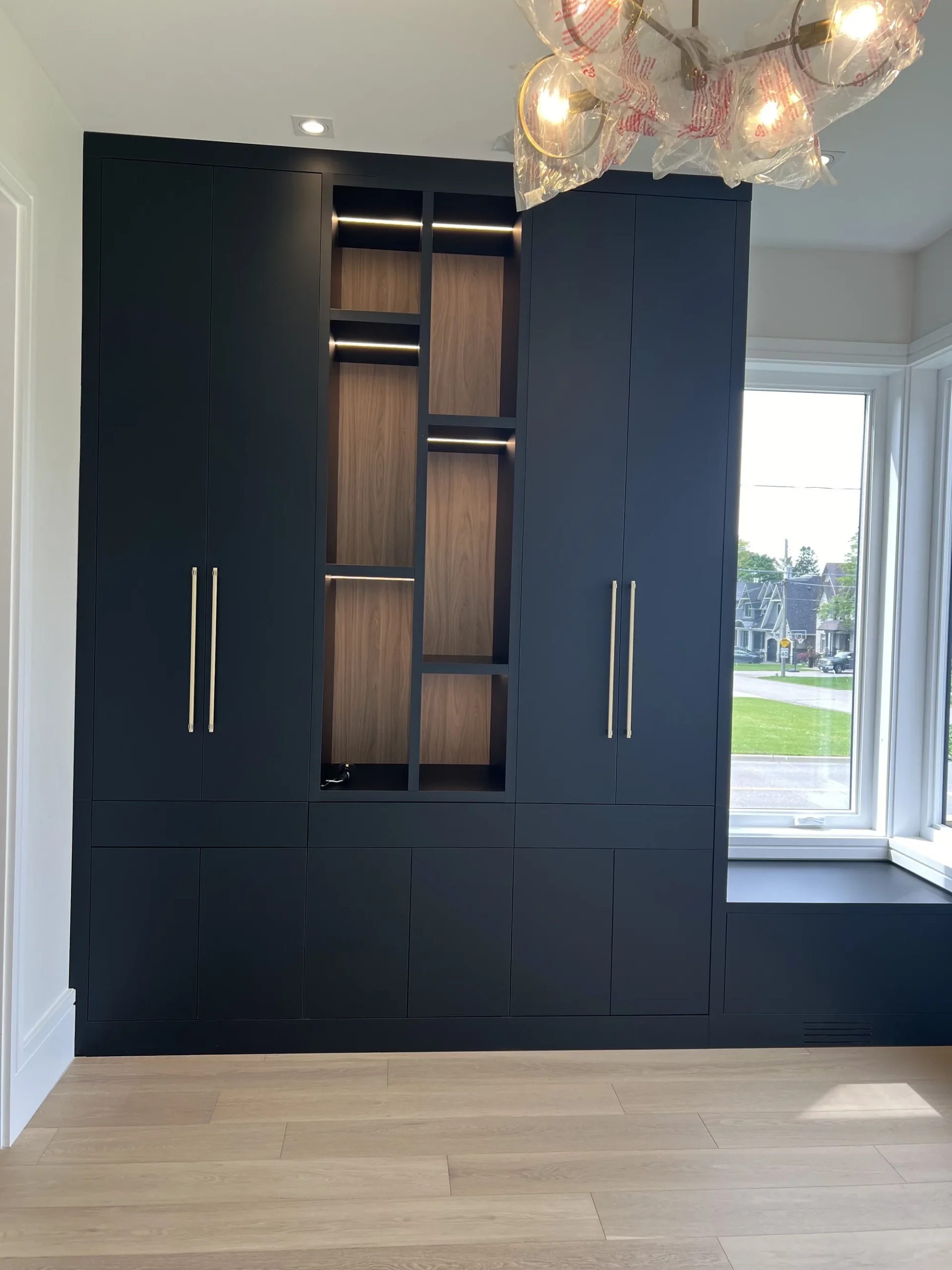 Canadian-Made Custom Cabinetry & Built-In Furniture 4 Canadian-made cabinetry in an Ontario home: a navy built-in wall unit with brass pulls, a lit walnut display centre and a window seat.