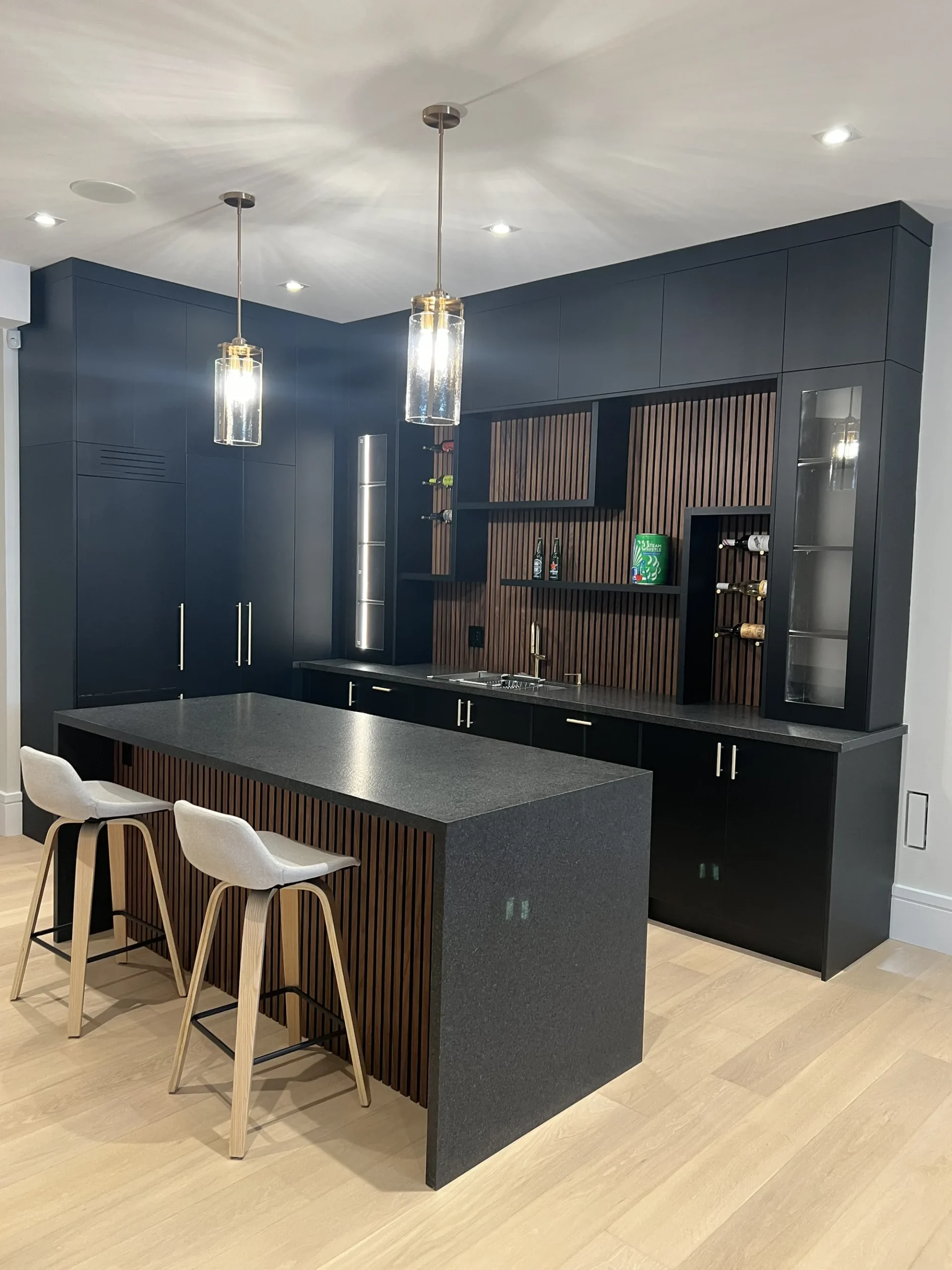 Coffee bar cabinets in an Ontario home: black bar cabinetry with a fluted walnut island, glass display towers and a built-in tap.