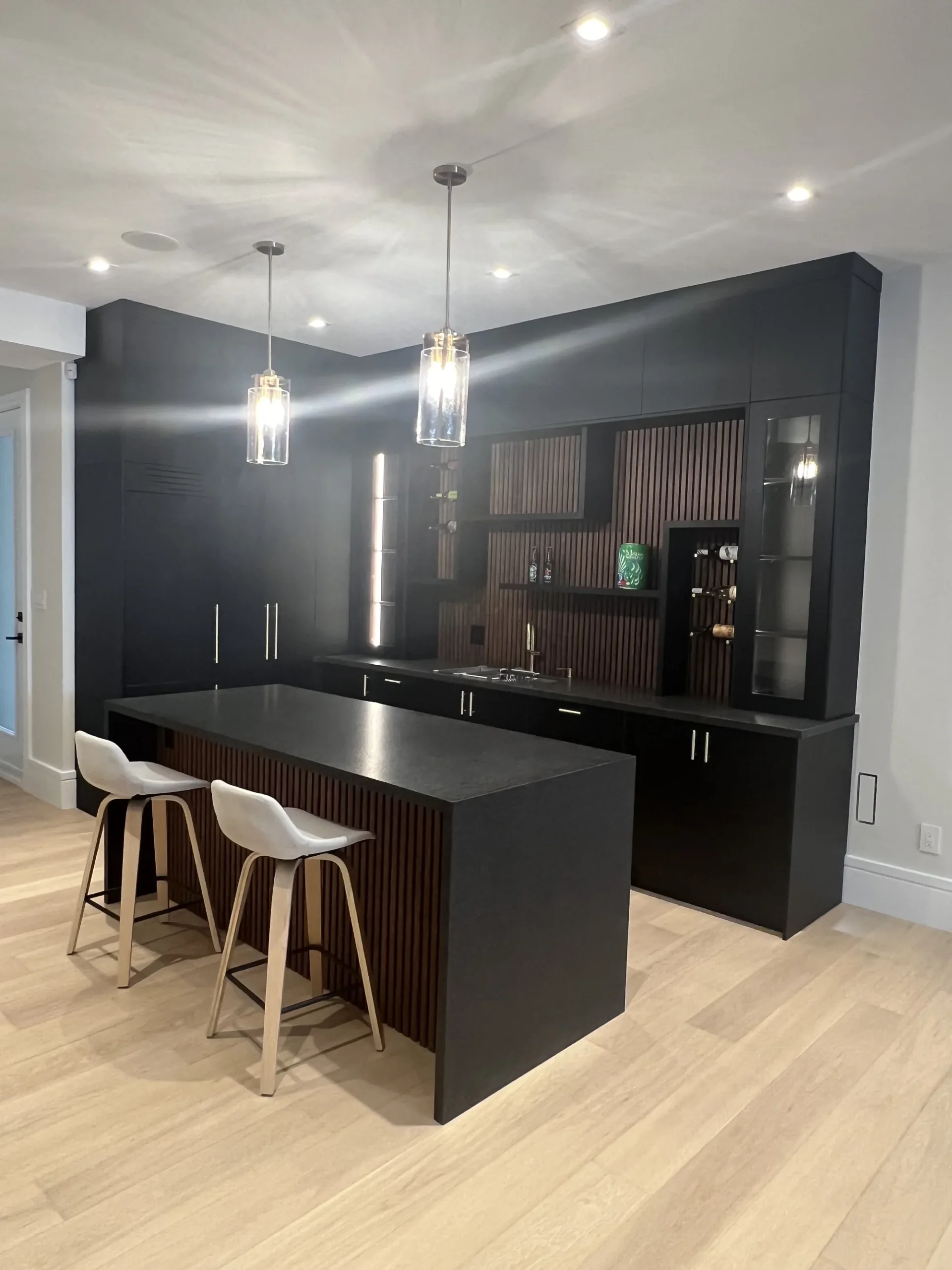 Coffee bar cabinets in an Ontario home: a black bar wall with lit glass display towers over a fluted walnut back panel.