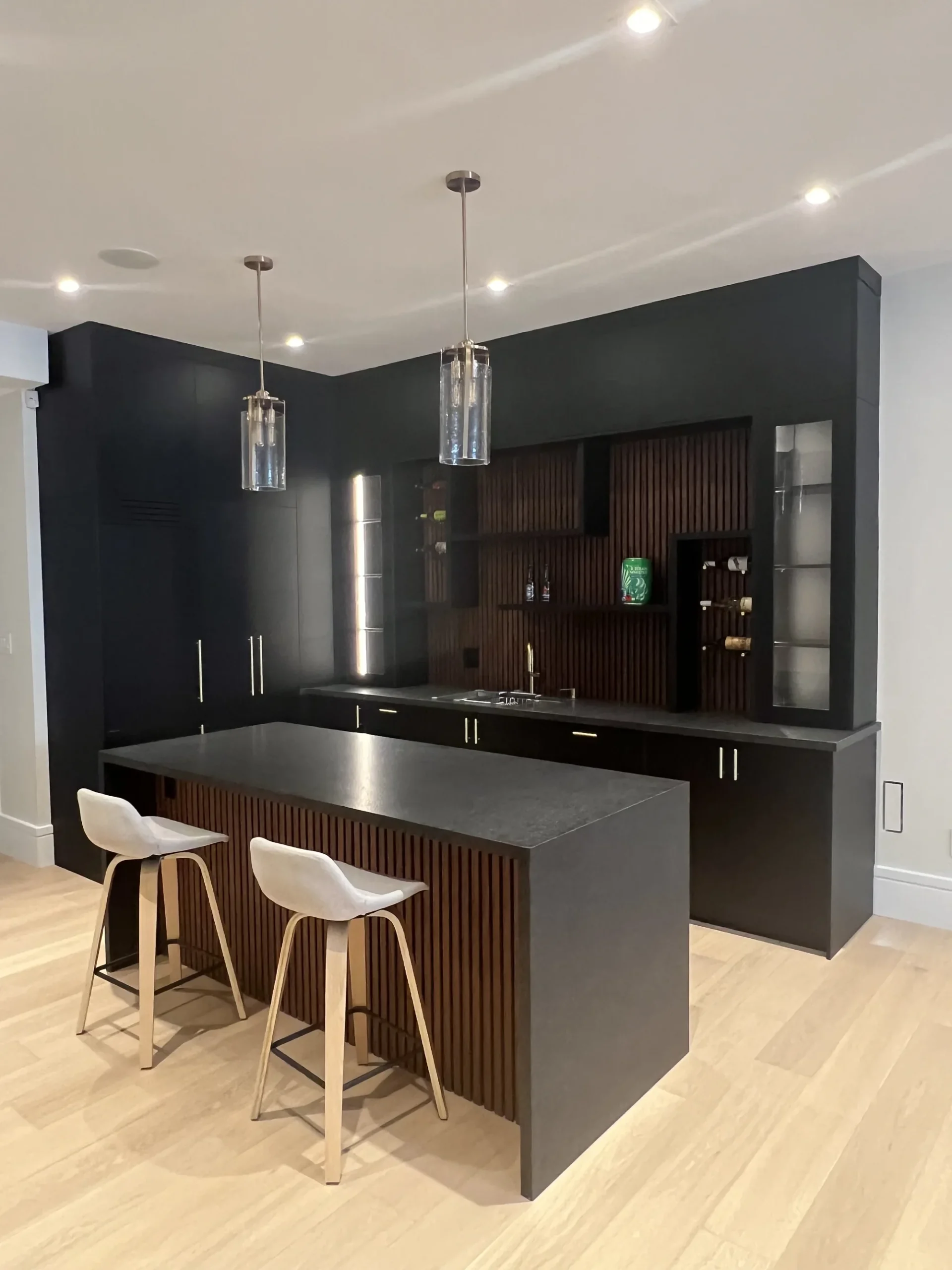 Coffee bar cabinets in an Ontario home: a fluted walnut island with a stone top and counter stools, facing a black bar wall.
