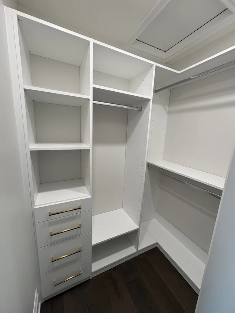 Custom closets in an Ontario home: a walk-in with a four-drawer tower on brass pulls, open shelving above and long hanging opposite.