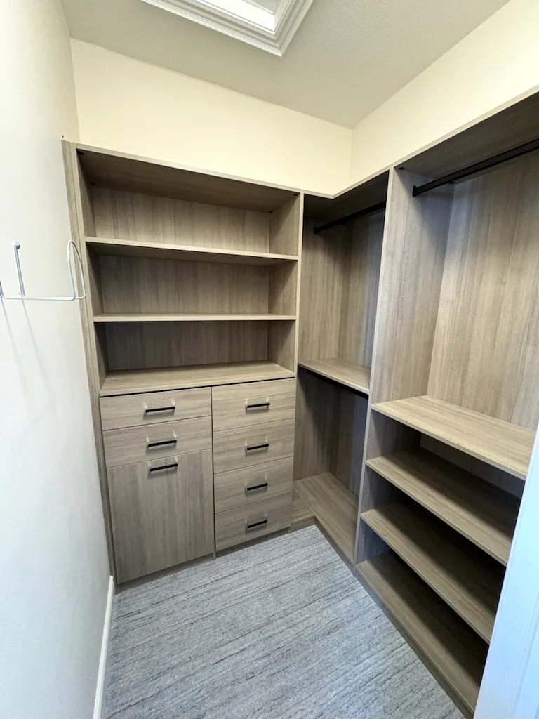 Custom closets in an Ontario home: a walk-in in a greige woodgrain finish with open shelving, a drawer bank and shoe shelves.