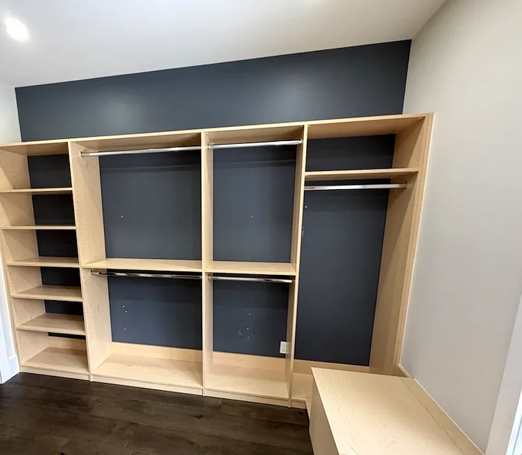 Custom closets in an Ontario home: a maple walk-in with navy back panels, high-low hanging and a built-in window bench.