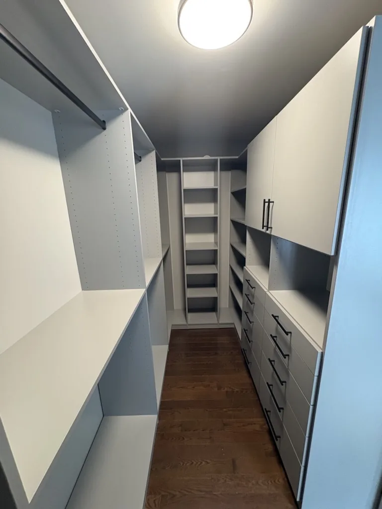 A custom walk-in closet in an Ontario home with two-tone shelving, a double-hang rail, a bank of drawers and a corner shelf tower.