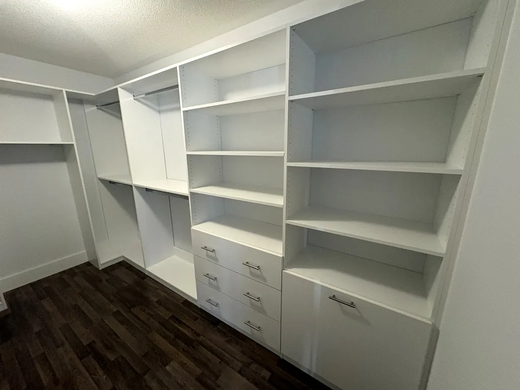 A custom walk-in closet in an Ontario home with a deep open shelf tower, a bank of drawers and corner hanging rails.