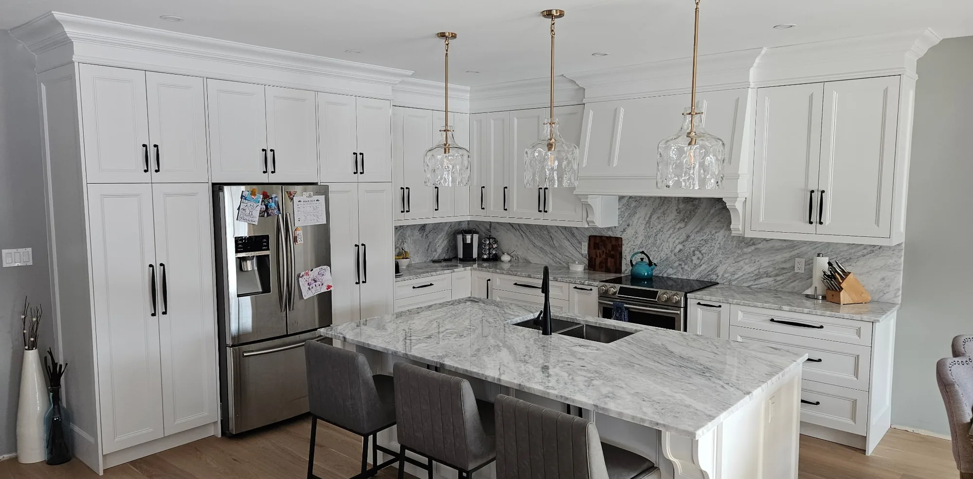 Custom kitchen cabinets in an Ontario home: a floor-to-ceiling white shaker cabinet run, marble-look counters and backsplash, and a seated island.